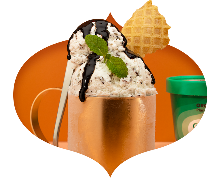 Mint chip ice cream scoops coming out of a copper mug, topped with fresh mint, waffle cone and chocolate sauce